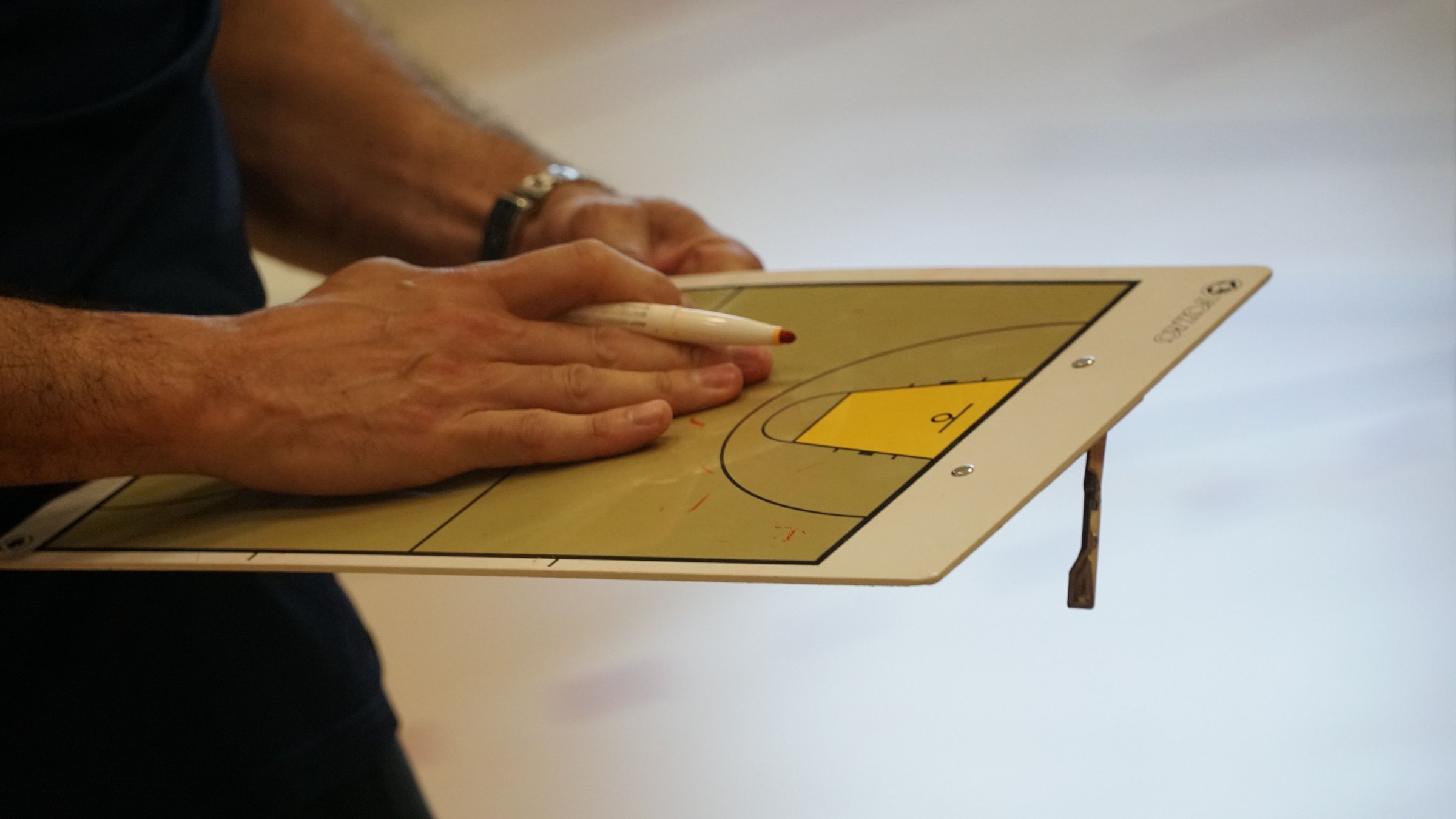 A hand writing on a coach's court board with a marker, the board resting across a forearm.