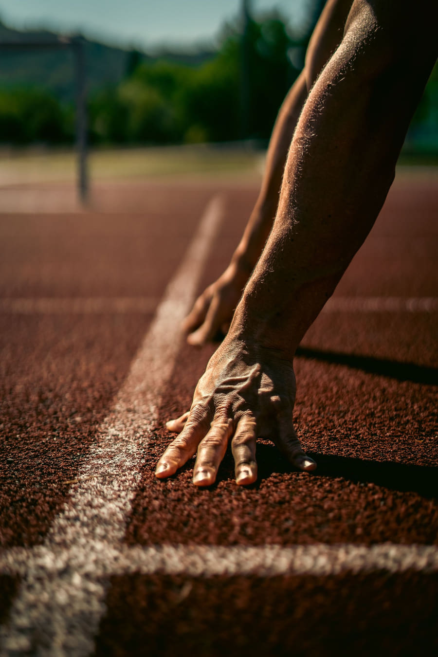 A hand pressed flat on the white start line of a red running track, close up.